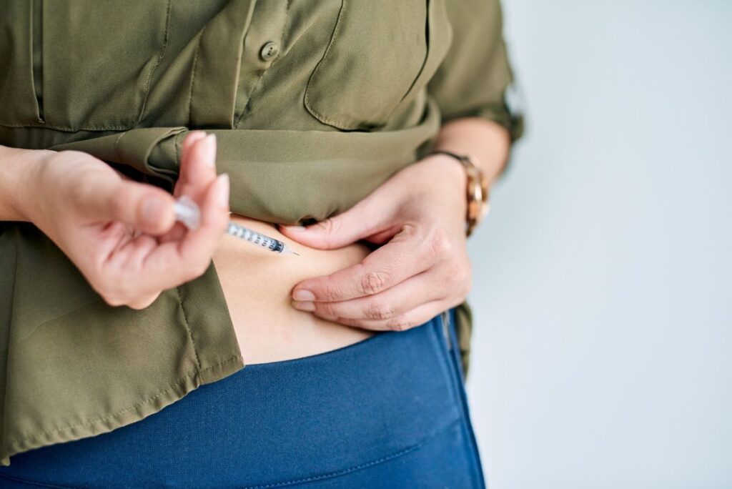 Woman, hands and insulin injection in stomach, diabetes treatment and medicine on studio background. Female person