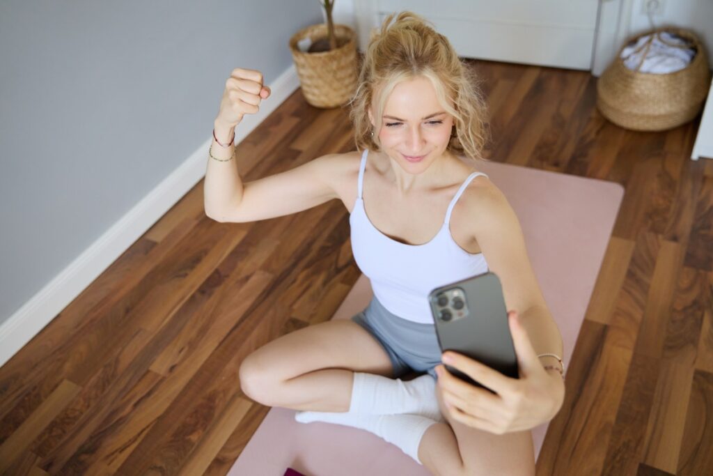 young woman takes selfies on smartphone while sitting on rubber mat at home